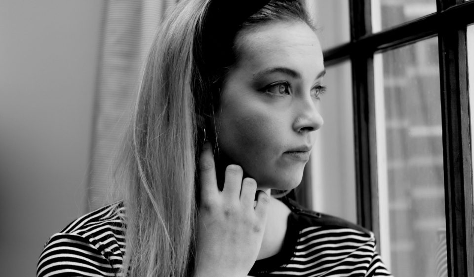 Femme pensive près d'une fenêtre, la main sur la nuque