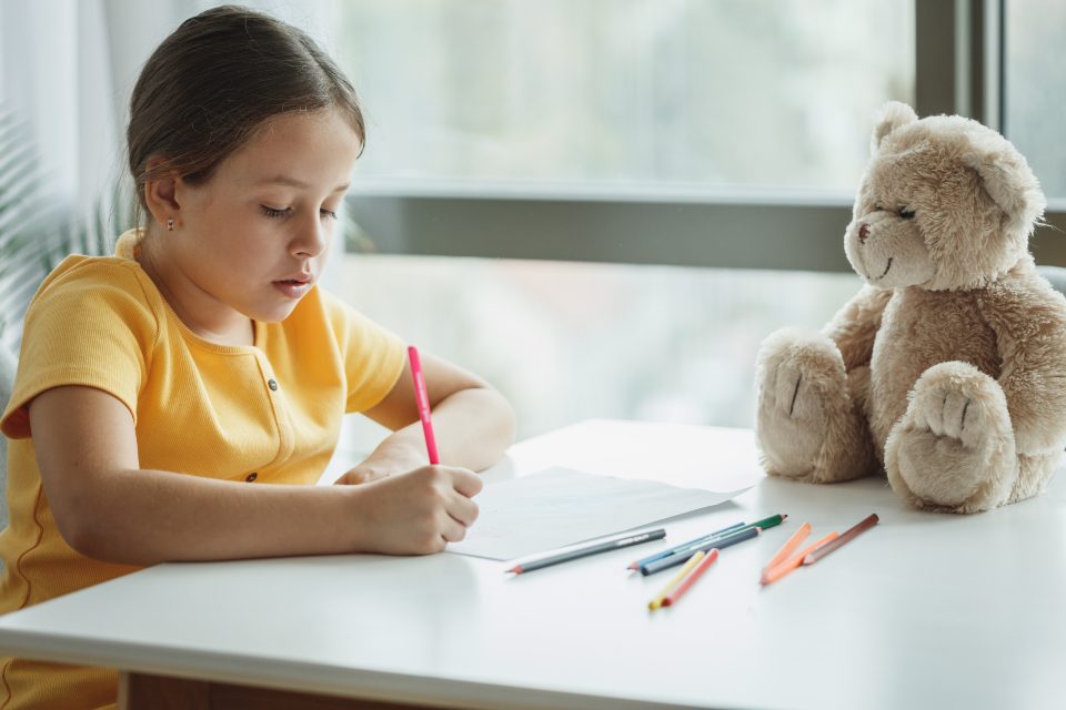 Petite fille qui dessine à côté de son ours en peluche