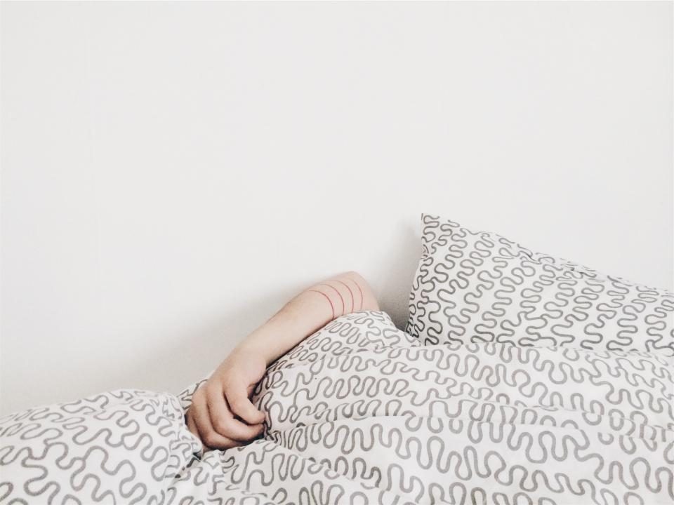 Main qui dépasse de la couette dans un lit